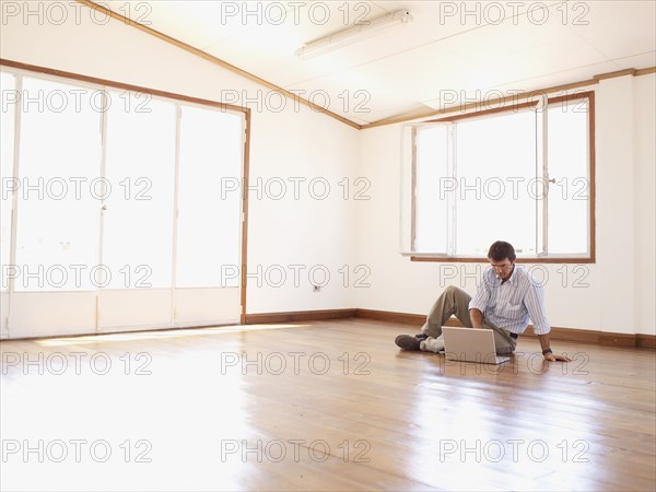 Hispanic businessman using laptop on floor in empty office