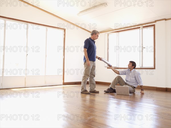 Hispanic businessman handing paperwork to co-worker in empty office