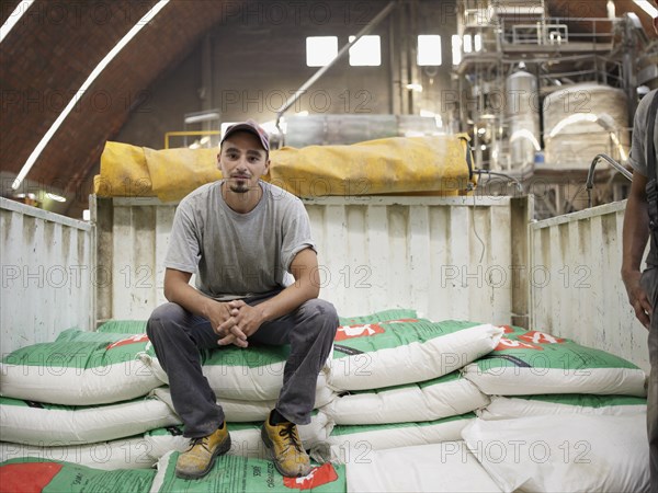 Hispanic worker sitting on bag in factory