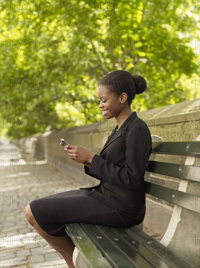 African businesswoman looking at cell phone on bench