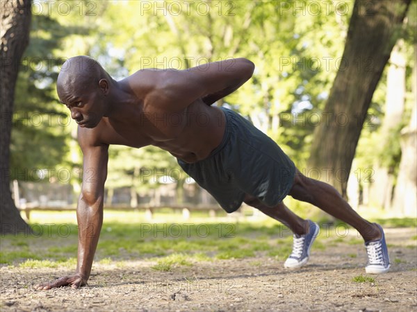 African man doing one arm push-ups in park