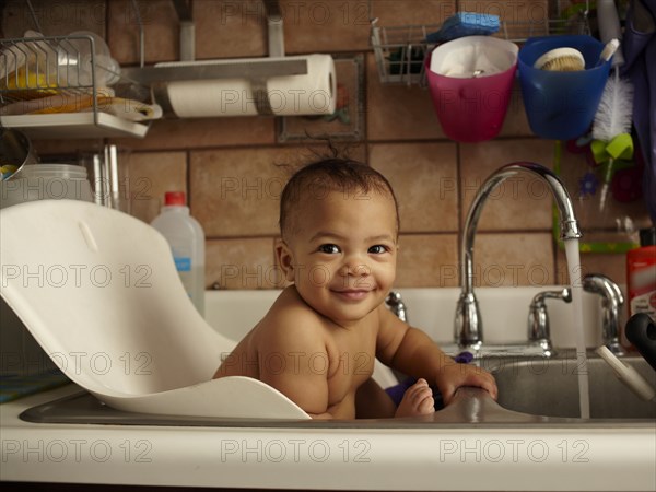 Mixed race baby girl bathing in sink