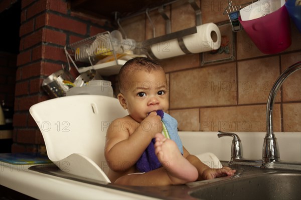 Mixed race baby girl bathing in sink