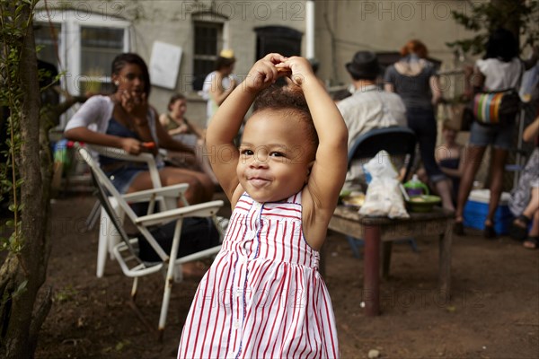 Mixed race baby girl standing on patio with arms raised