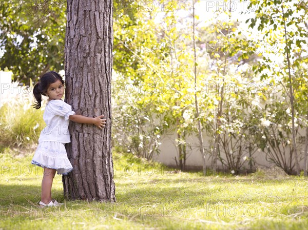 Hispanic girl hugging tree trunk