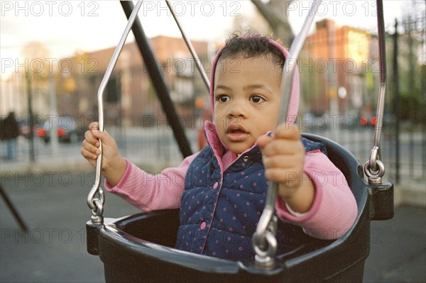 Mixed race girl swinging in playground