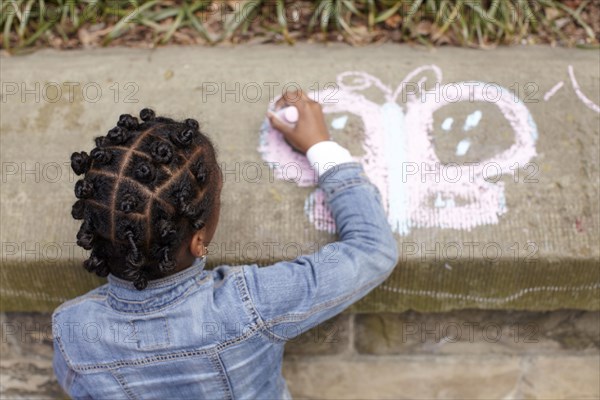 Mixed race girl drawing on cement with chalk