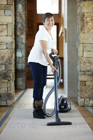 Older Hispanic woman vacuuming carpet