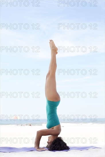 Mixed race woman practicing yoga on beach