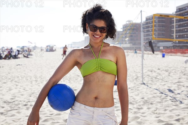 Hispanic woman holding volleyball on beach