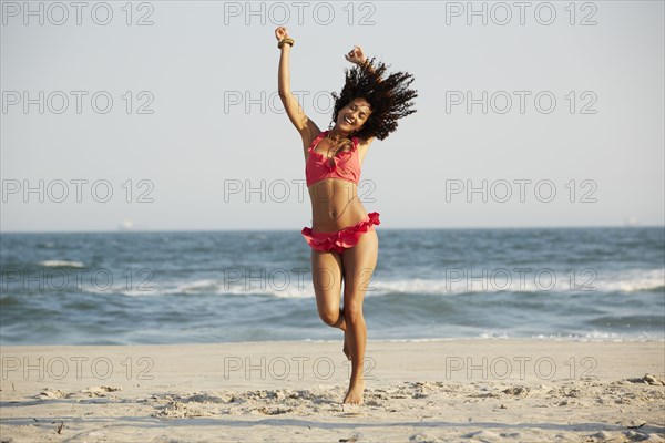 Mixed race woman jumping for joy on beach