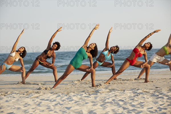 Women practicing yoga on beach