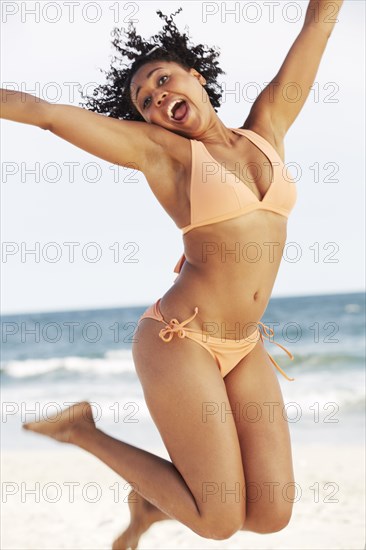 Mixed race woman jumping for joy on beach