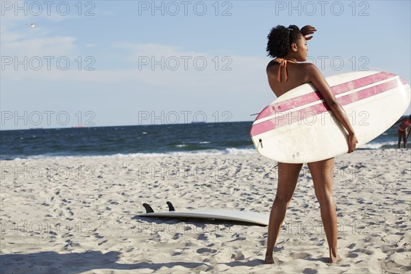 Mixed race woman carrying surfboard on beach