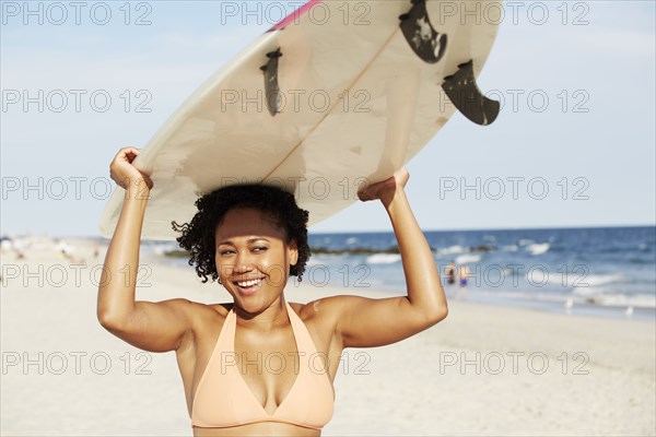 Mixed race woman carrying surfboard on beach