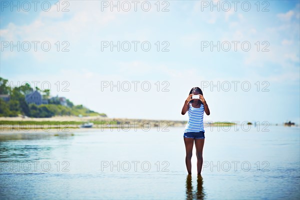 Black teenage girl taking photograph on beach