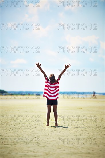 Black girl standing with arms raised on beach