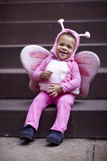 Mixed race girl wearing pink butterfly Halloween costume on staircase