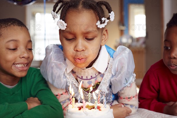 Black girl blowing out cake candles at party