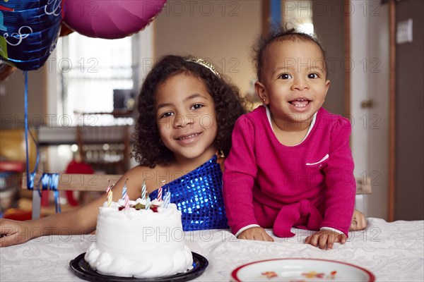 Mixed race sisters smiling with cake at party