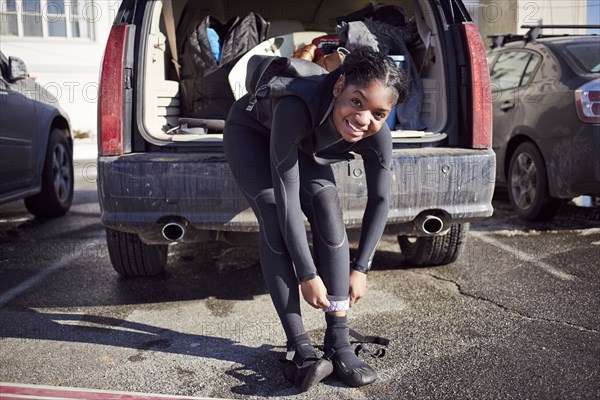 Black teenage girl putting on wetsuit