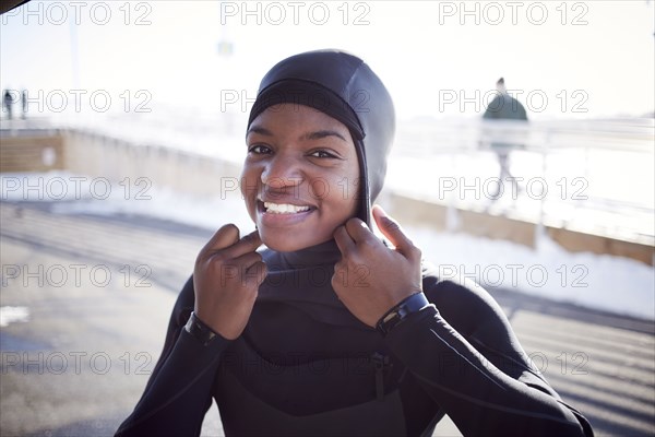 Black teenage girl putting on wetsuit swimming cap