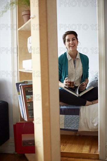 Woman drinking tea and reading in bedroom