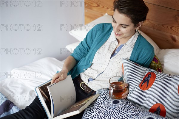 Woman drinking tea and reading in bed