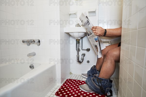 Mixed race man reading newspaper on toilet