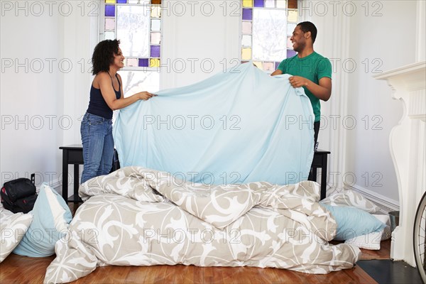 Couple changing sheets on bed