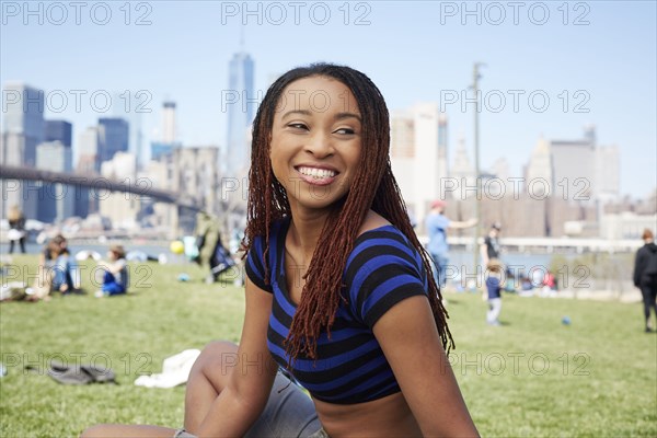 Smiling Black woman sitting in grass at waterfront