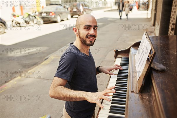 Hispanic man playing piano on city sidewalk