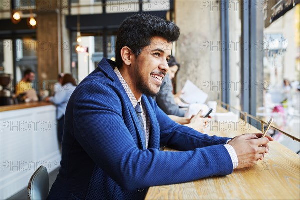 Smiling Middle Eastern man using cell phone at cafe window