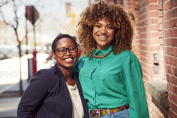 Smiling Black women posing on city sidewalk