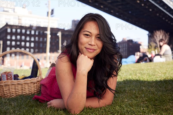 Pacific Islander woman laying on grass with picnic basket