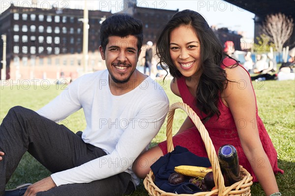 Couple sitting on grass with picnic basket
