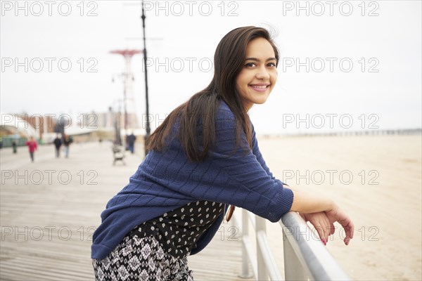 Smiling Mixed Race woman leaning on boardwalk railing