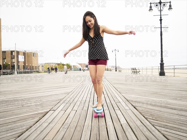 Mixed Race woman riding skateboard on boardwalk