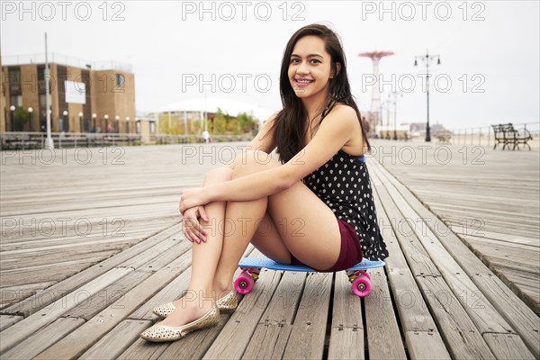 Mixed Race woman sitting on skateboard on boardwalk