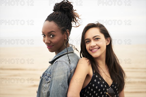 Smiling women back to back on beach