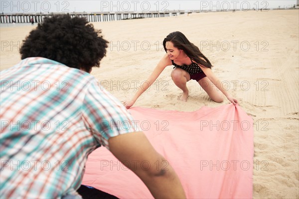 Couple spreading blanket on beach