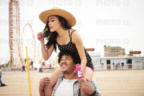 Man carrying woman blowing bubbles on shoulders at beach