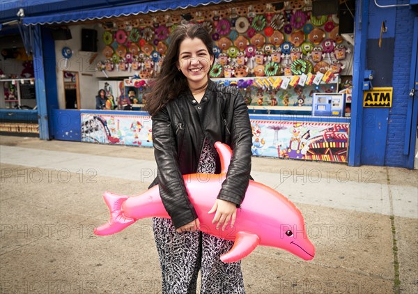 Mixed Race woman holding pink inflatable dolphin at amusement park