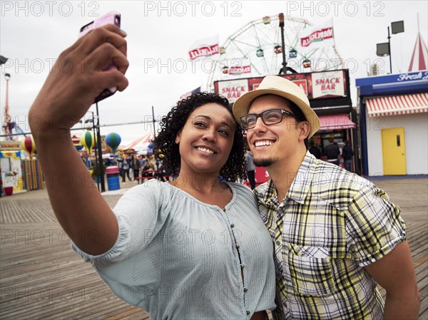 Couple posing for selfie on boardwalk at amusement park