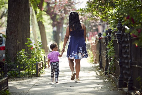 Mother walking daughter on city sidewalk