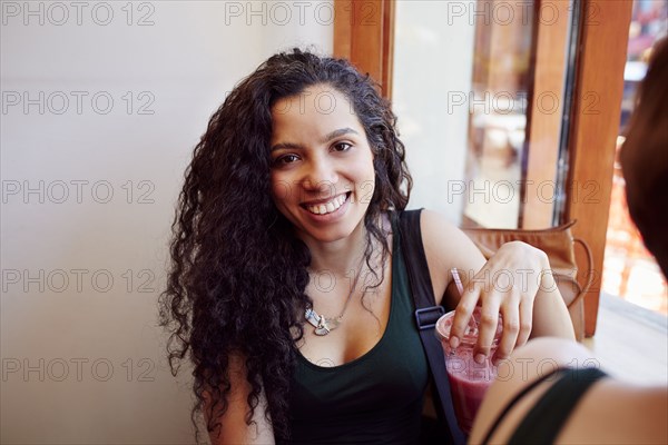 Smiling Black woman drinking smoothie in cafe