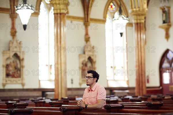 Kneeling Hispanic man praying in church pew