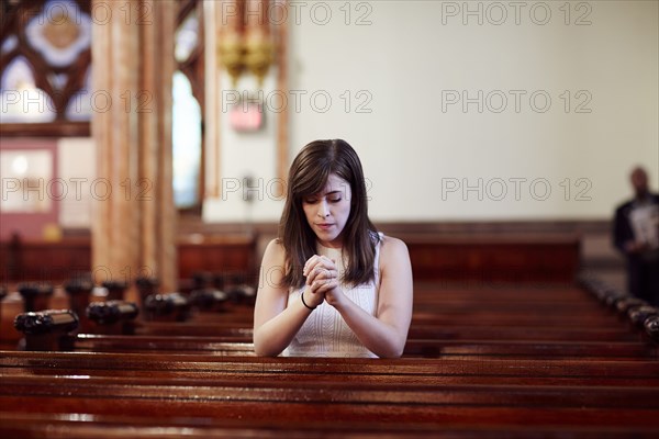 Kneeling Caucasian woman praying in church pew