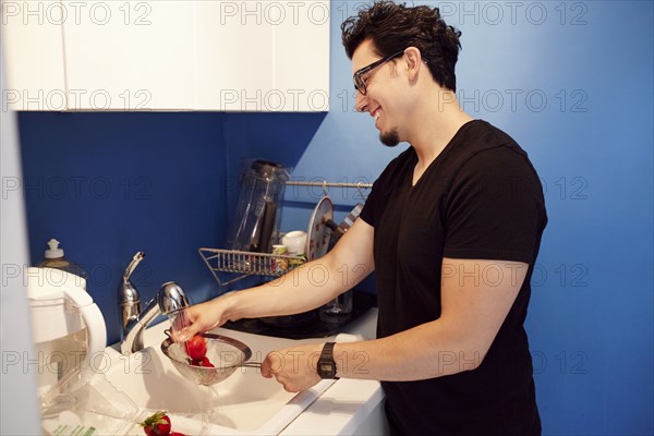 Hispanic man washing strawberries in sink