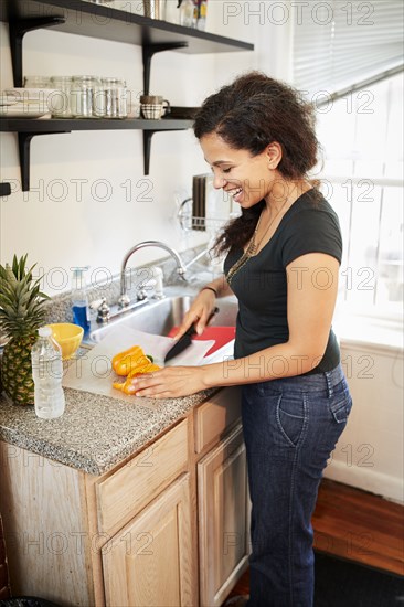 Smiling Mixed Race woman chopping pepper on cutting board